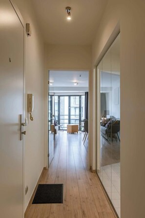A hallway leading to a living area with a glass partition, a wooden floor, and a door with a phone. - Cozy 2BR unit w/ kitchen & TV (Knokke-Heist)