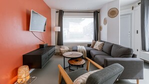Ein modernes Wohnzimmer mit einer Couch, einem an der Wand montierten Fernseher, einem kleinen runden Tisch und einer Lampe.