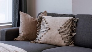 Ein modernes Wohnzimmer mit einem grauen Sofa, einer beige farbenen Decke und zwei gewebten Wanddekorationen.