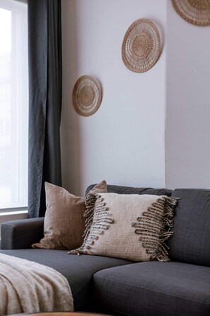 A modern living room with a grey sofa, a beige throw blanket, and two woven wall decorations. - Knokke retreat near the coast w/ full kitchen (Knokke-Heist)