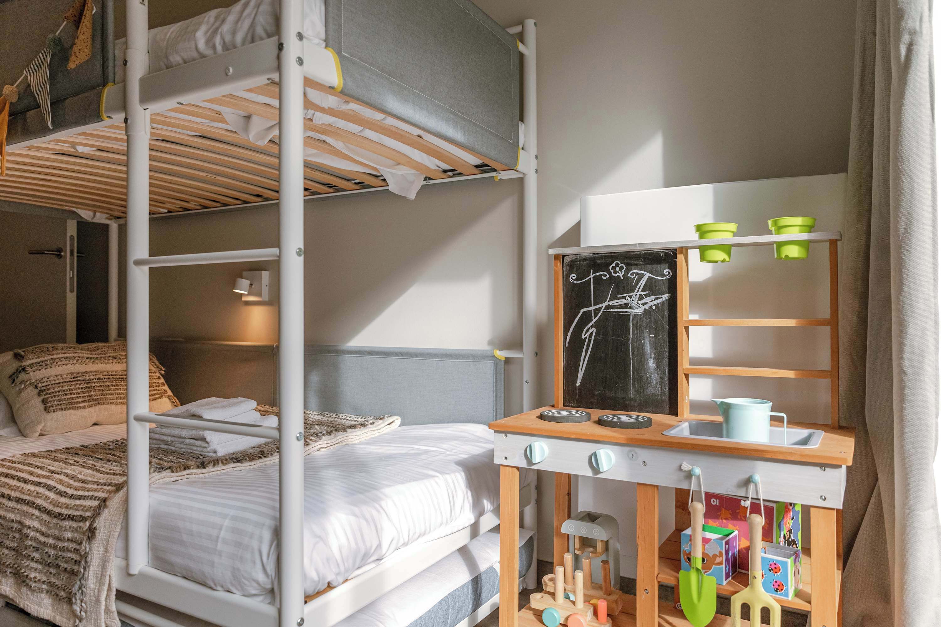 Ein Schlafraum mit Etagenbett, Schreibtisch, einer Tafel und Kinderspielzeug.