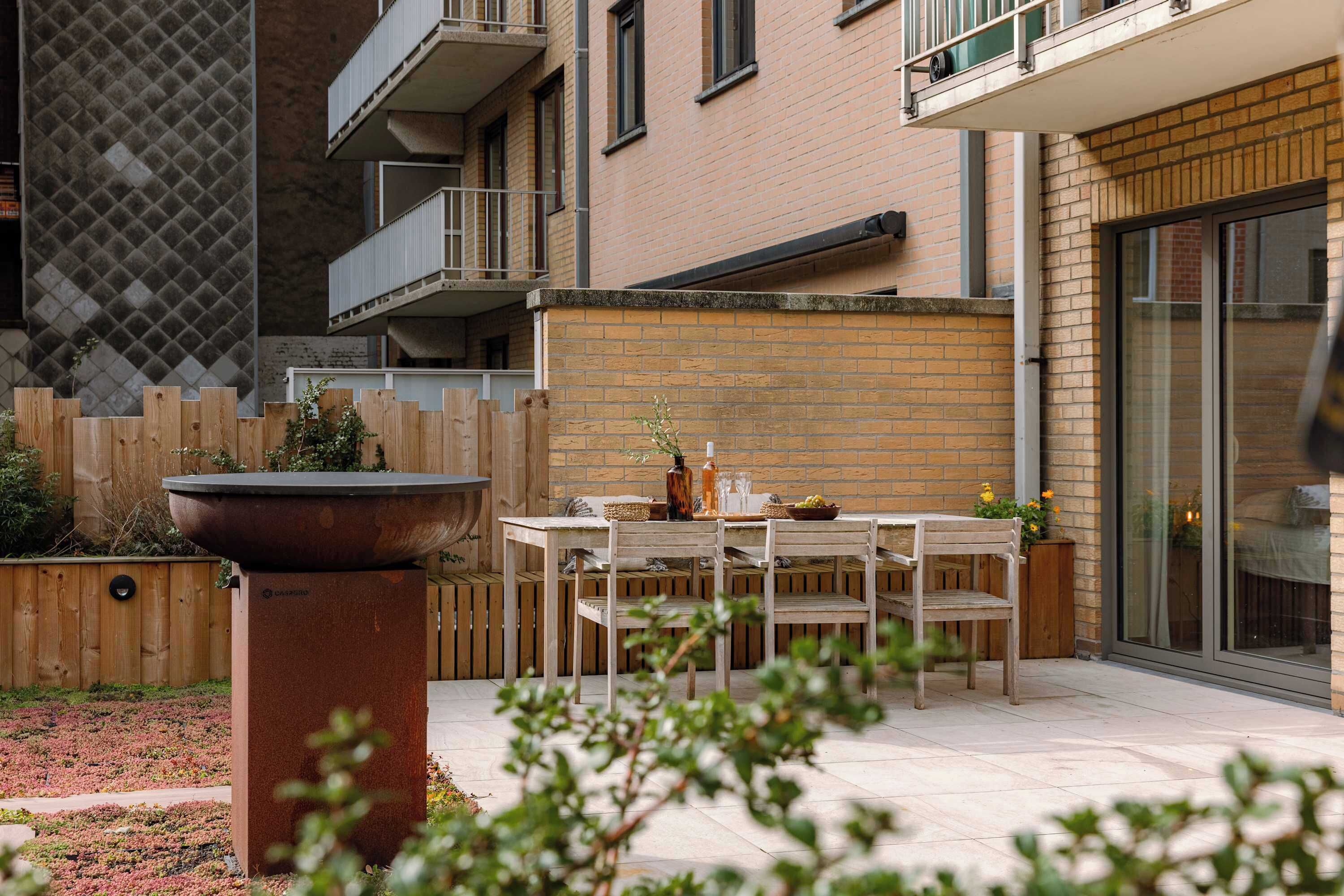 A patio with a table and chairs, a wooden fence, and a brick building with a balcony.