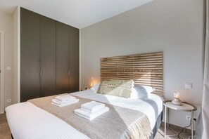 Un dormitorio con una cama grande, un armario, una mesita de noche con una lámpara y un cabecero.