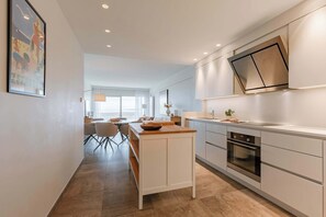 Una cocina moderna con una isla central, horno empotrado y un comedor con mesa y sillas.
