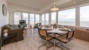 A modern living room with a dining area, large windows, and a view of the sea. - Casiola waterfront apt - garage & sea views (Oostende)