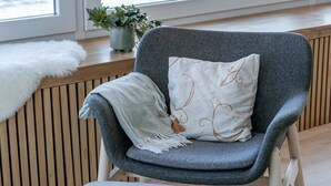 A grey armchair with a cushion, a matching ottoman, a white furry throw, and a potted plant by a window with a view of the sea. - Casiola waterfront apt - garage & sea views (Oostende)