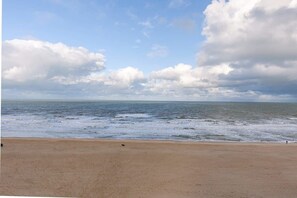 Ein Strand mit weitem Sandstreifen und Blick auf das Meer unter bewölktem Himmel.