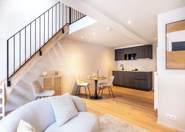 A modern living room with a staircase, a dining area, and a kitchen.