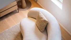 A modern, curved sofa with a textured pillow and a matching throw pillow, placed on a light-colored rug in a room with wooden flooring and a window. - Light-filled duplex w/ workspace & TV (Gent)