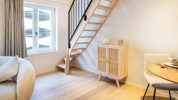 A modern living room with a wooden staircase, a dining area, and a large window. - Light-filled duplex w/ workspace & TV (Gent)