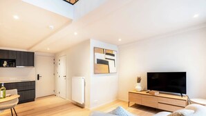 A modern living room with a sofa, a TV, a dining area with a table and chairs, and a kitchen in the background. - Light-filled duplex w/ workspace & TV (Gent)