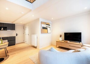 Un salon moderne avec un canapé, un téléviseur, un coin repas comprenant une table et des chaises, et une cuisine en arrière-plan.