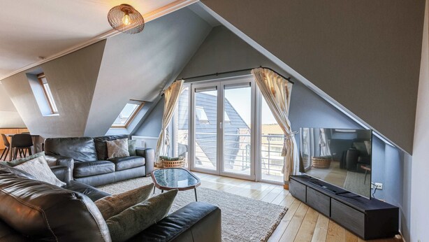 Ein Wohnzimmer im Loft-Stil mit großem Fenster, einer Couch, einem Couchtisch und einem Flachbildfernseher.