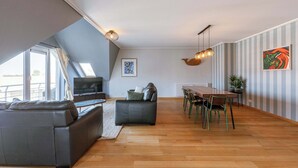 Ein modernes Wohnzimmer mit einer Couch, einem Esstisch mit Stühlen, einem Fernseher und einer Deckenleuchte.