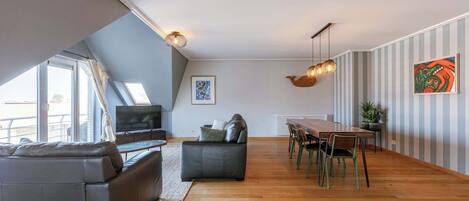 Una sala moderna con un sofá, una mesa de comedor con sillas, un televisor y una lámpara en el techo.