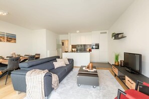 Ein modernes Wohnzimmer mit Sofa, Couchtisch, Fernseher und einem Essbereich mit Stühlen und Tisch.