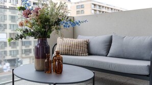 A balcony with a sofa and a table, a vase with flowers, and a cityscape view. - Charming 2BR apartment w/ kitchen & workspace (Oostende)