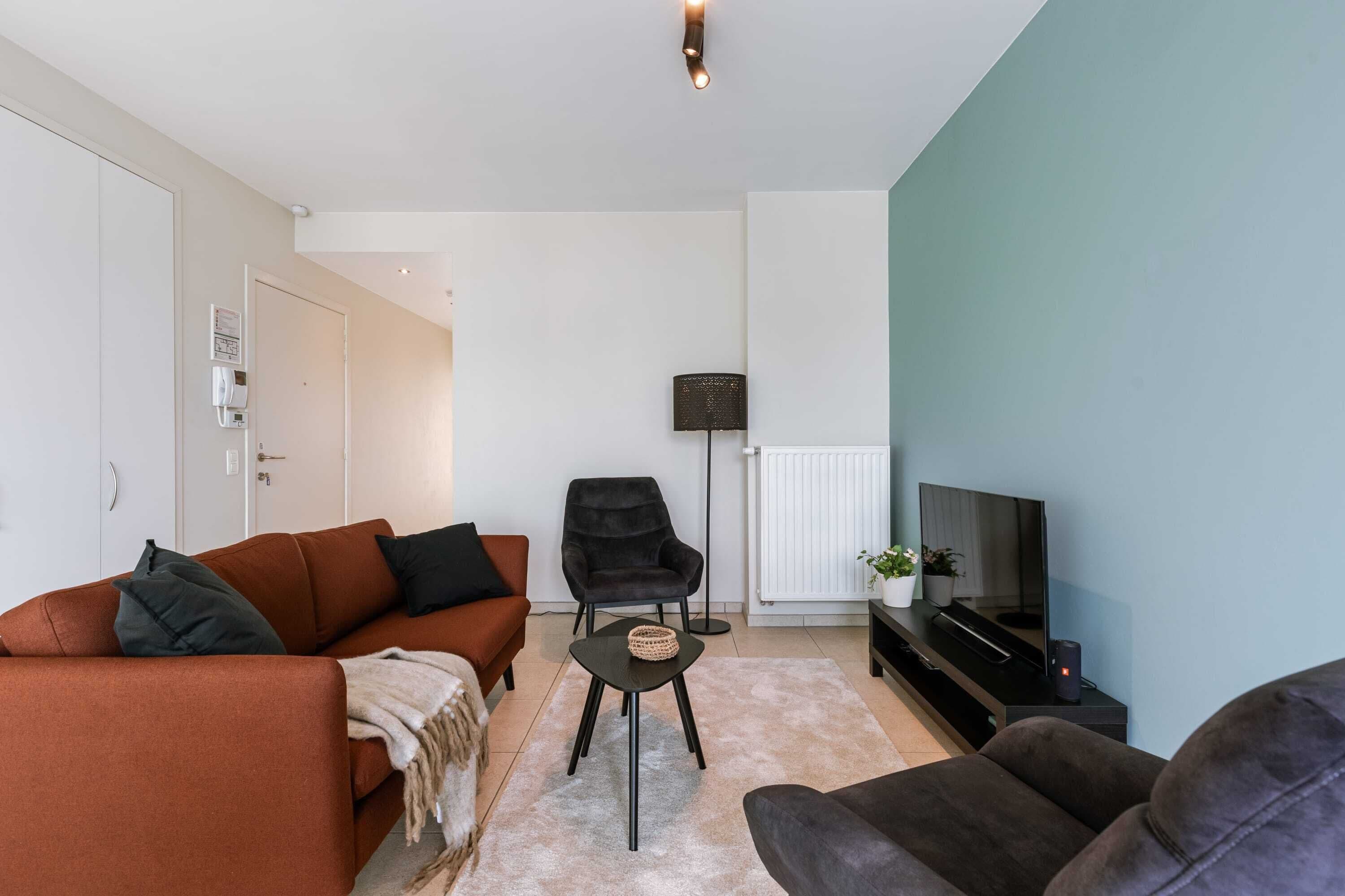 Ein Wohnzimmer mit einer Couch, einem Sessel, einem Fernseher und einem kleinen Tisch.