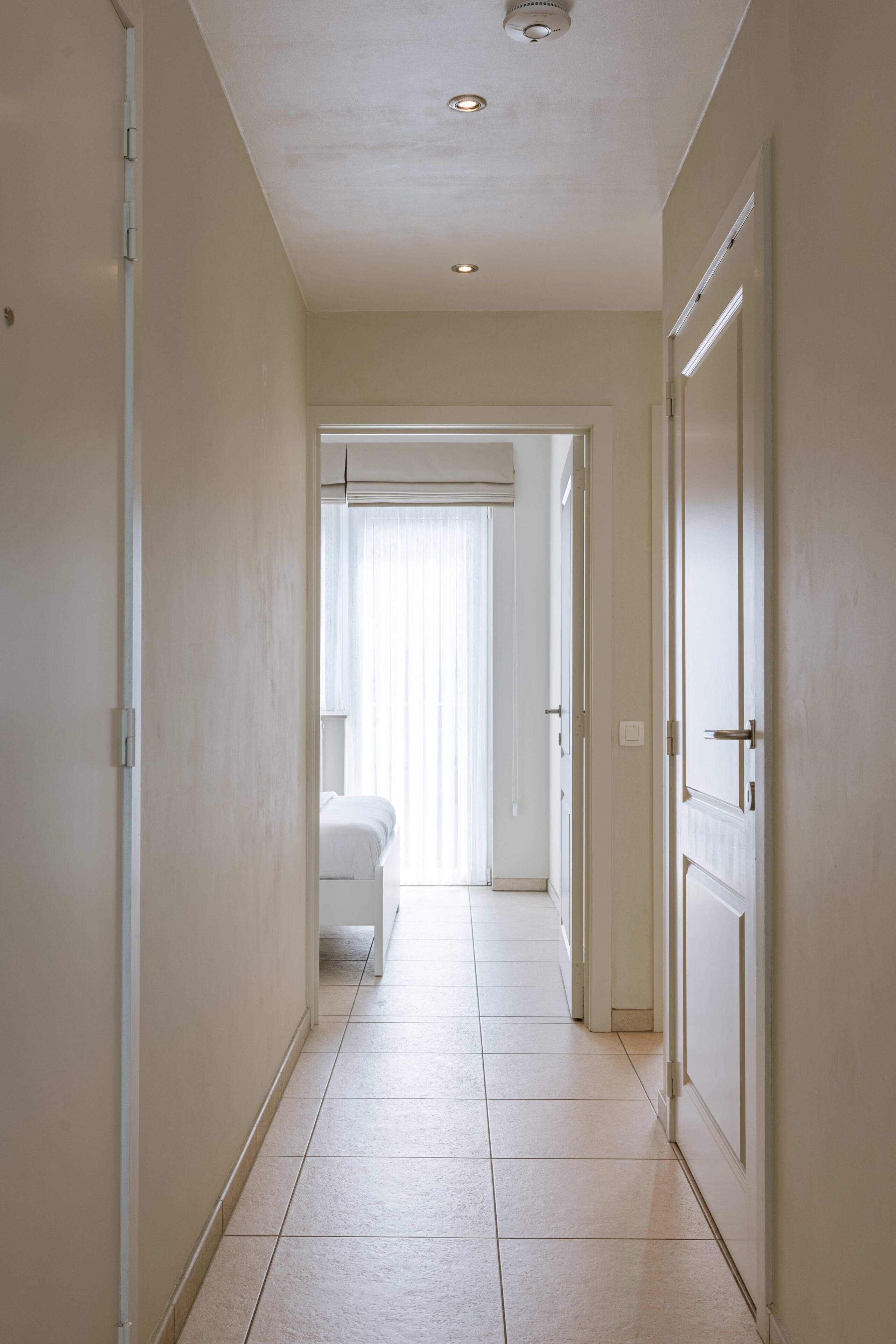 A hallway with a tiled floor, white walls, and doors leading to rooms.