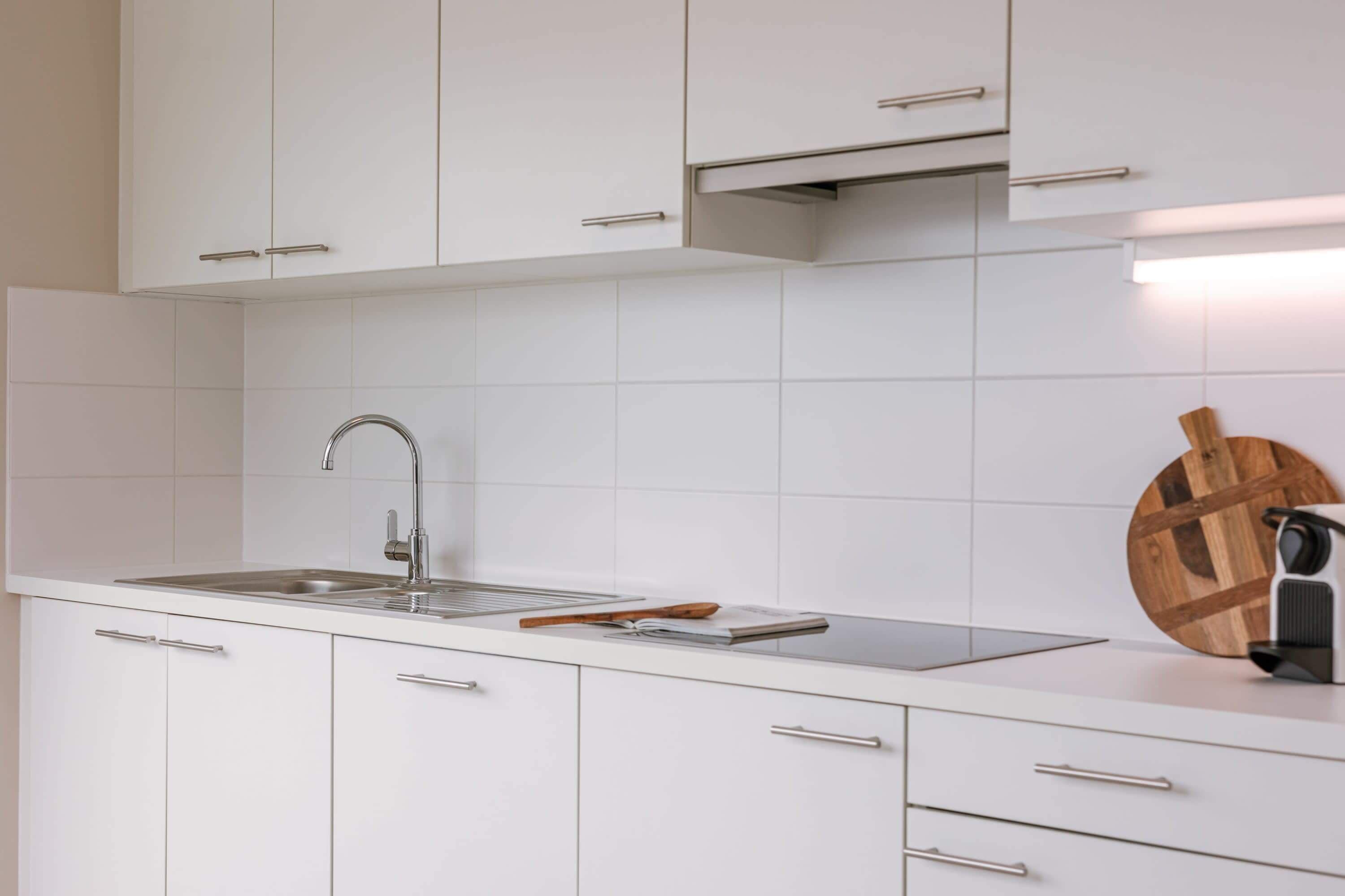A modern kitchen with white cabinets, a stainless steel sink, and a wooden cutting board.