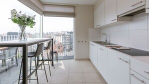 A modern kitchen with a large window, a dining area with chairs, and a view of the cityscape. - Cozy 2BR apartment w/ workspace & TV (Oostende)