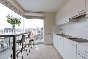 Eine moderne Küche mit einem großen Fenster, einer Essecke mit Stühlen und Blick auf die Stadt.