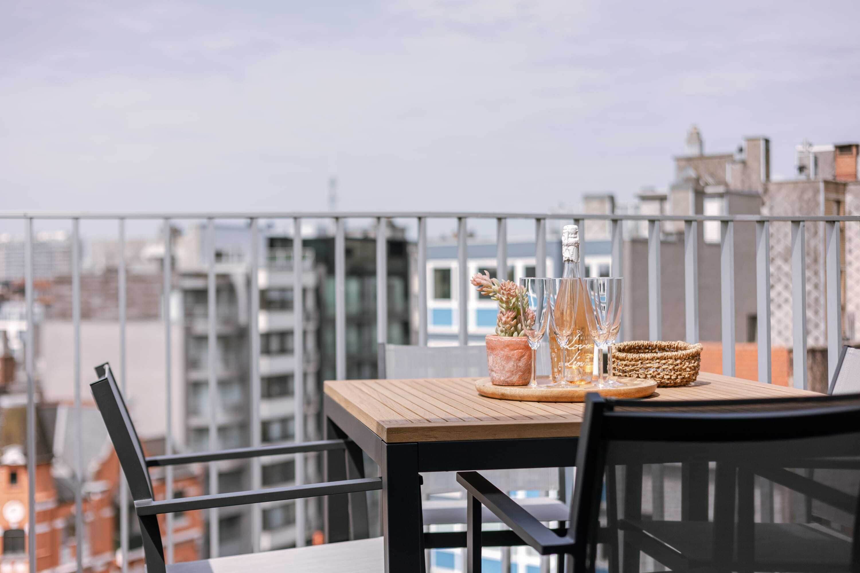 Un balcon avec une table en bois, deux chaises, une plante en pot et un panier tressé.