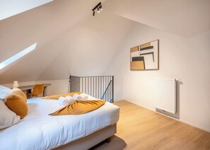 Una camera da letto moderna con soffitto spiovente, un letto con biancheria bianca, una coperta gialla senape e un termosifone.