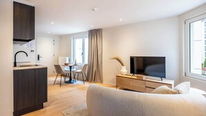 Ett modernt hotellrum med ett litet kök, en matplats, en stor säng, en TV och utsikt över staden.