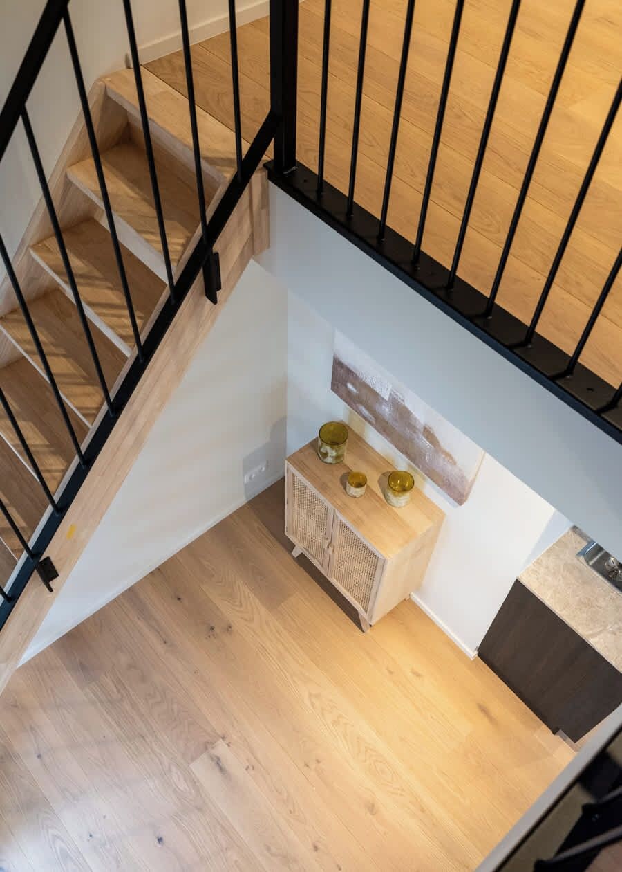 Eine Holztreppe mit schwarzen Geländern, die zu einer Ebene weiter unten führt.