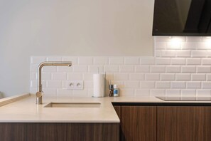Eine moderne Küche mit Edelstahlarmatur, weiß gefliestem Fliesenspiegel und Holzschränken.