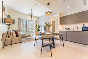 A modern living room with a sofa, dining table, and chairs, a kitchen with cabinets, and a large window. - Sophisticated 2BR Retreat Featuring Fountain Views, Moments from Burj Khalifa (Dubai)