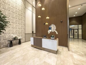 A reception area with a marble floor, a wooden reception desk, a wall with a brick pattern, and hanging pendant lights. - Sophisticated 2BR Retreat Featuring Fountain Views, Moments from Burj Khalifa (Dubai)