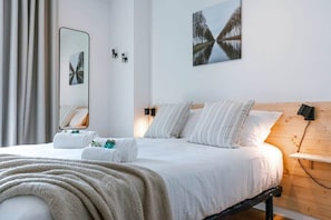 A modern hotel room with a bed, a mirror, a painting, and a wooden headboard.