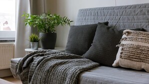 A bed with a grey quilt, two grey pillows, a grey knitted blanket, and a potted plant on a bedside table. - Historic apartment w/ kitchen (Gent)