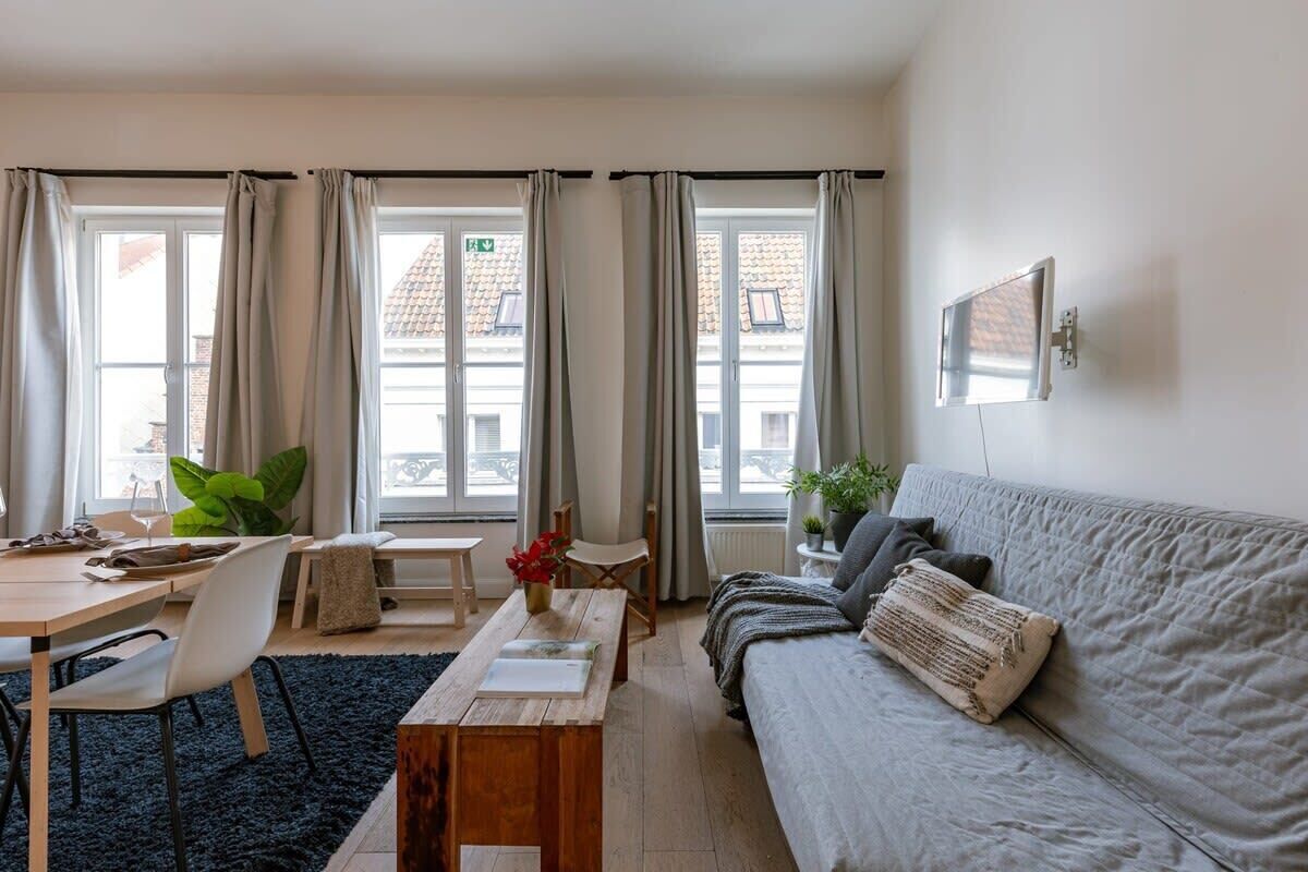 Bright living room with natural light and minimalist decor featuring a wooden coffee table and wall-mounted television.