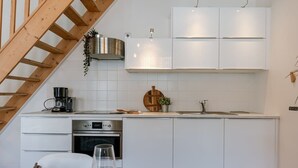 A modern kitchen with white cabinets, a wooden staircase, and a dining area with a table and chairs. - Historic apartment w/ kitchen (Gent)