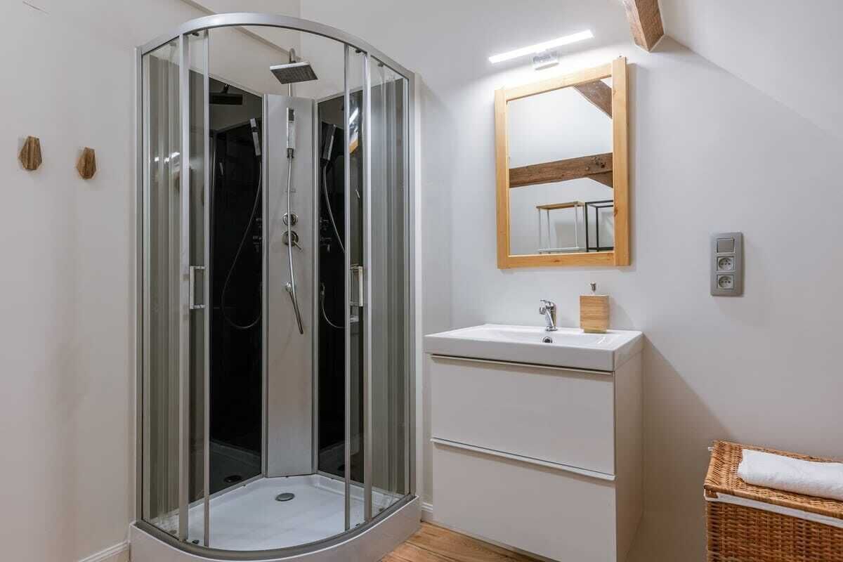 A modern bathroom with a glass-enclosed shower, a white sink, a mirror, and a wicker basket.