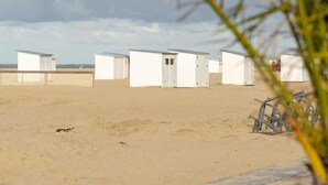 En sandstrand med hvide strandhuse og et hegn i baggrunden.