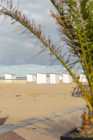 Ein sandiger Strand mit weißen Strandhütten und einem Zaun im Hintergrund.