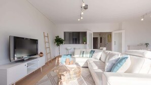En moderne stue med et fladskærms-tv, hvide sofaer, et sofabord og et stort vindue.