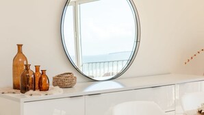 Et hvidt toiletbord med et rundt spejl, et vindue med udsigt og pynteting på bordet.