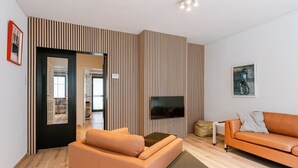 Een moderne woonkamer met een bank, een salontafel, een televisie en behang met strepen.
