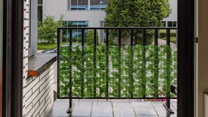 Een balkon met uitzicht op een modern gebouw, een boom en een metalen hek.