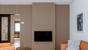 Een moderne woonkamer met een flatscreen televisie bevestigd aan een houten lambrisering, een bank en een salontafel.