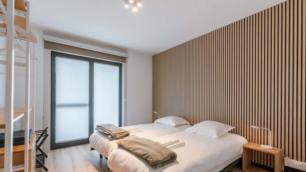 Een moderne slaapkamer met een groot bed, een wand van houten latten, een klein nachtkastje en een inbouwkast.