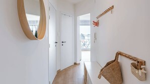 Een gang met houten vloer, een ronde spiegel, een plafondlamp en een wandrek met tassen.