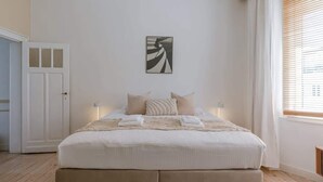 Ein Schlafzimmer mit Bett, einer Tür, einem Fenster mit Jalousien und einem Wandbild.
