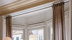 Ein Zimmer mit einer Couch, einem Tisch und Blick auf Gebäude durch große Fenster.