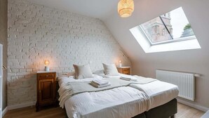 Et soveværelse med skråvæg, ovenlys, en murstensvæg, en seng med puder, sengeborde og en radiator.